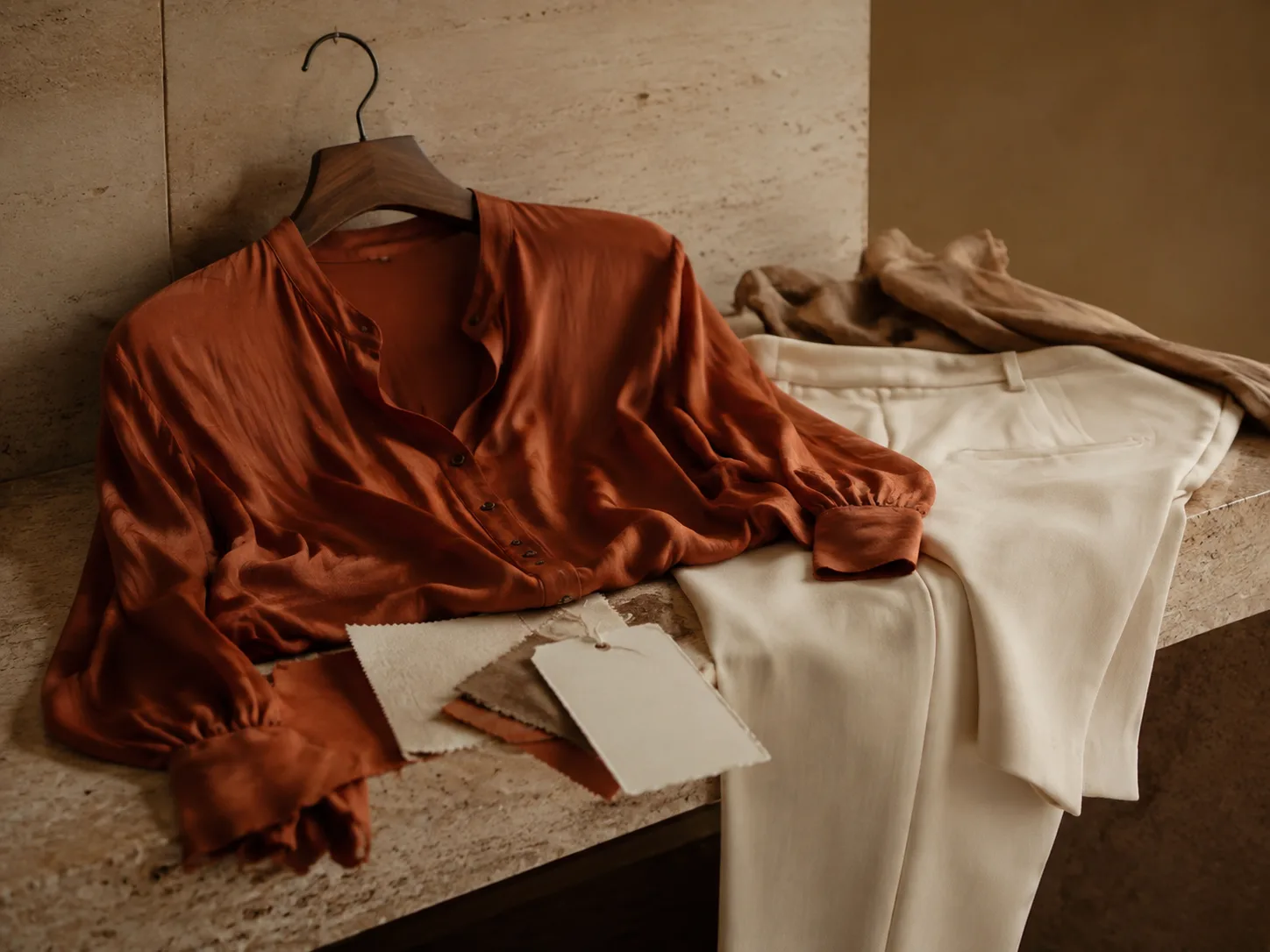 Rust silk blouse and ivory tailoring arranged with fabric swatches